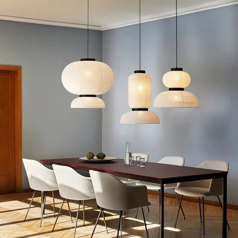 Three tiered white ribbed silk-paper lantern pendants with matte black wood collars suspended over a dark dining table with upholstered chairs