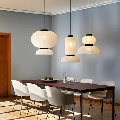Three tiered white ribbed silk-paper lantern pendants with matte black wood collars suspended over a dark dining table with upholstered chairs