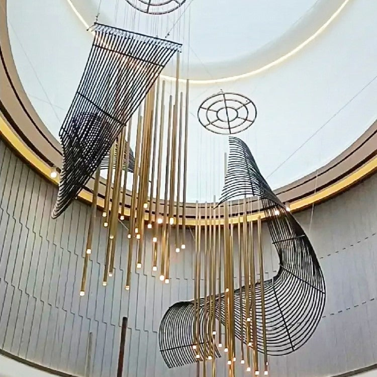 Full view of two sweeping black wire-ribbon canopies with vertical clusters of illuminated brass tube pendants in a circular hall