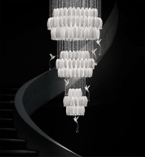 Three-tier cascading white glass plume chandelier accented with sculpted white birds in flight beside a curved staircase