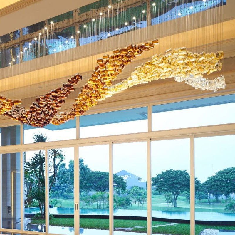 Close-up side view of the undulating wave chandelier showing gradient bronze, amber, and champagne gold glass cylinders