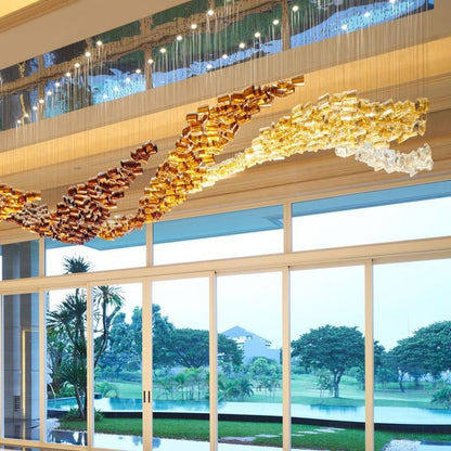 Close-up side view of the undulating wave chandelier showing gradient bronze, amber, and champagne gold glass cylinders
