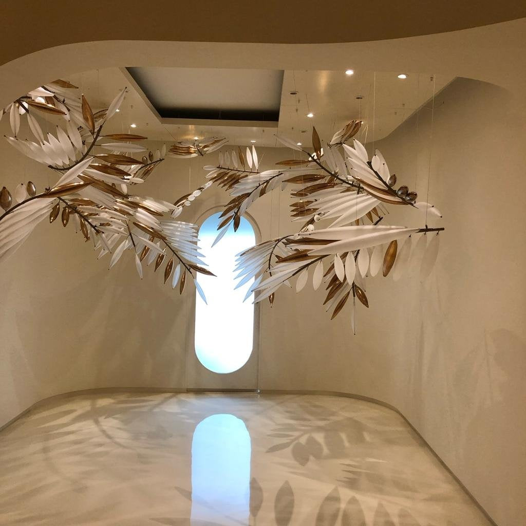 Sweeping overhead branches dressed with frosted white and metallic gold glass leaves suspended in a curved architectural foyer