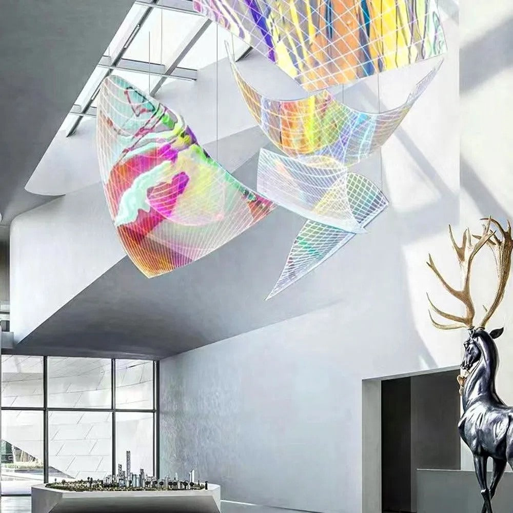Low-angle view of suspended iridescent wire-mesh sail panels glowing in magenta, yellow, and violet beneath a skylight
