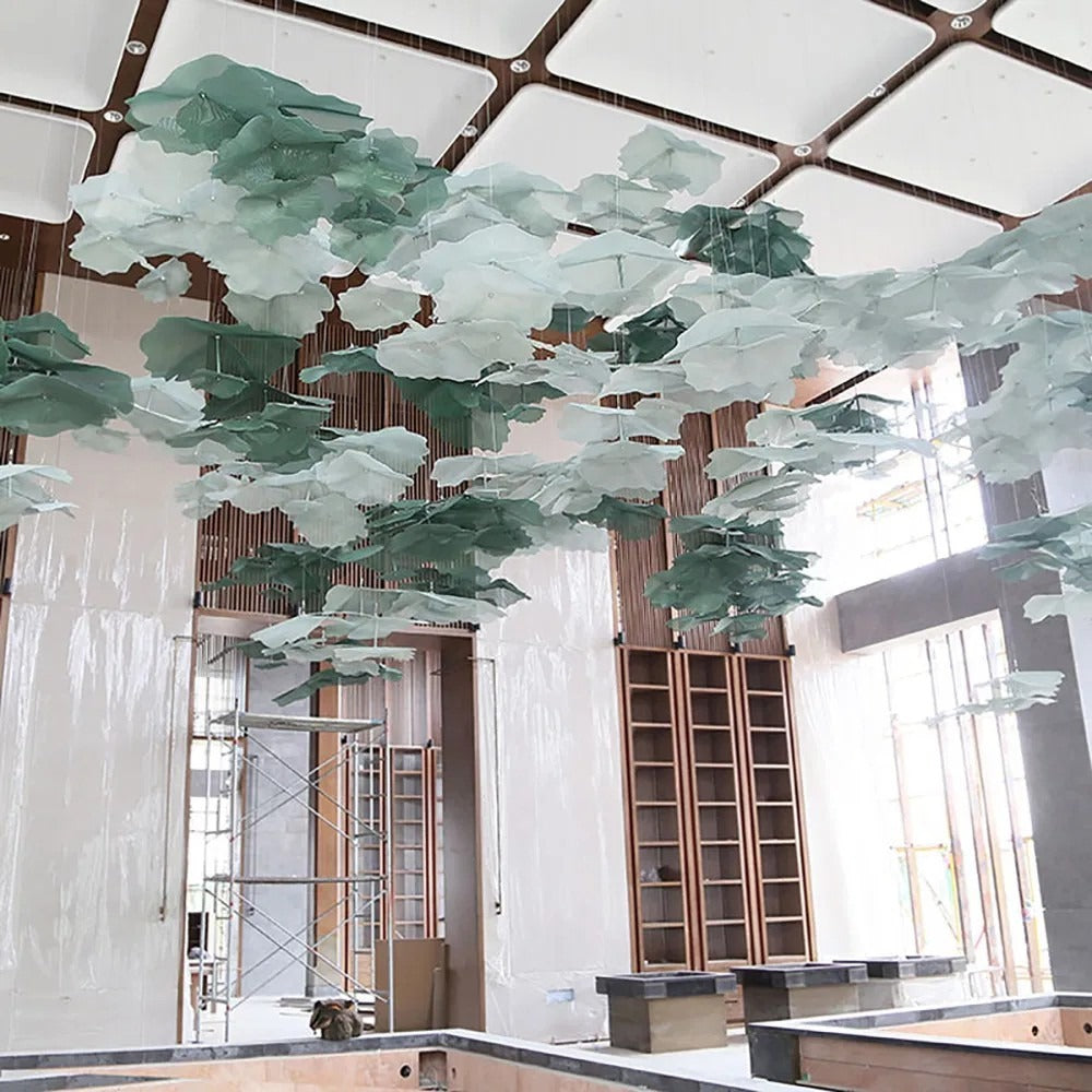 Wide view of a large ceiling installation of layered sage and emerald green perforated metal mesh lotus leaves in a high hall