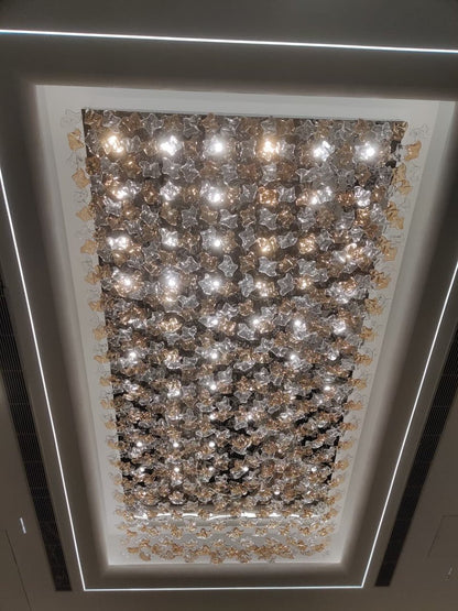 Directly upward view of a rectangular ceiling chandelier filled with clear and amber glass blossoms and integrated canopy downlights