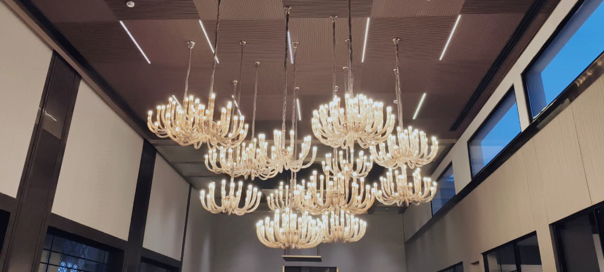 Cluster of amber glass candle-arm chandeliers hung at staggered heights under a slatted timber ceiling – Dasnac Westminster, Noida