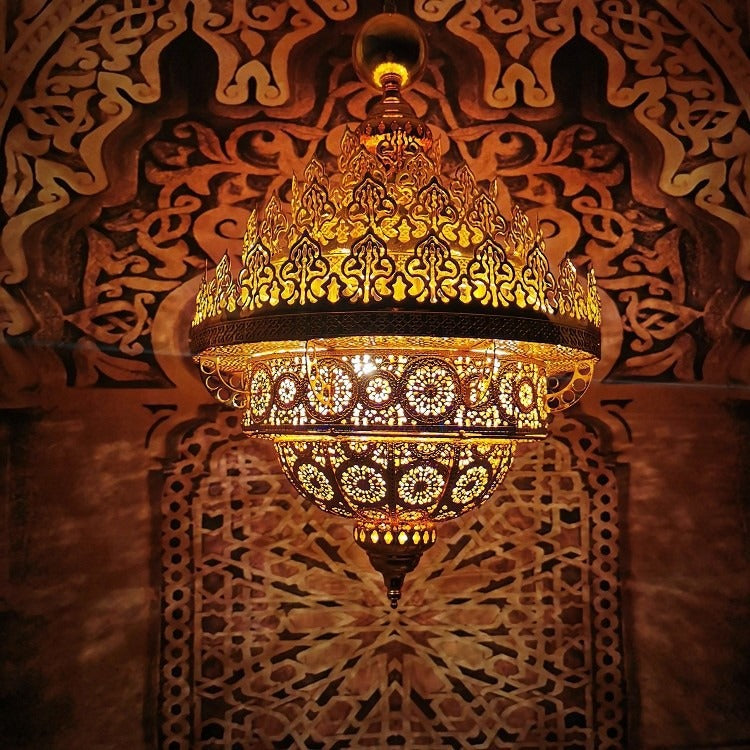 Illuminated pierced golden-brass dome chandelier casting intricate geometric jaali shadow patterns onto an arched wall