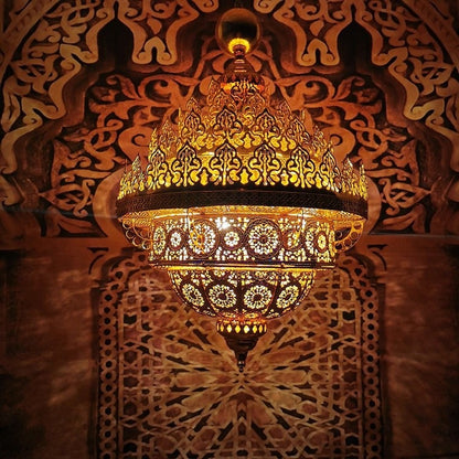 Illuminated pierced golden-brass dome chandelier casting intricate geometric jaali shadow patterns onto an arched wall