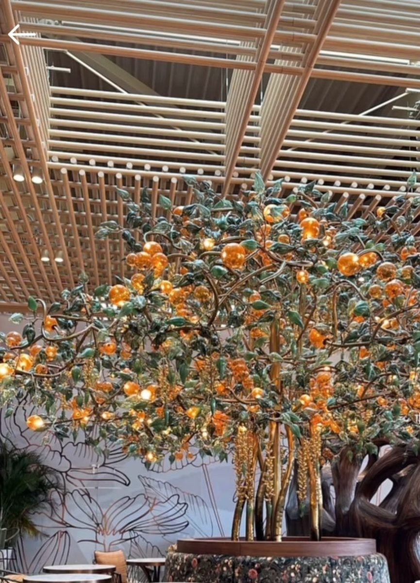 Sculptural tree lighting installation with golden metal trunks, green glass leaves, hanging golden clusters and glowing amber glass globes