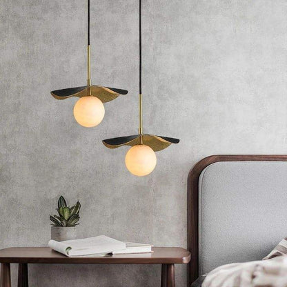 Staggered pair of sculpted bronze-and-brass lotus leaf pendant lights with glowing white alabaster globe diffusers beside a bed