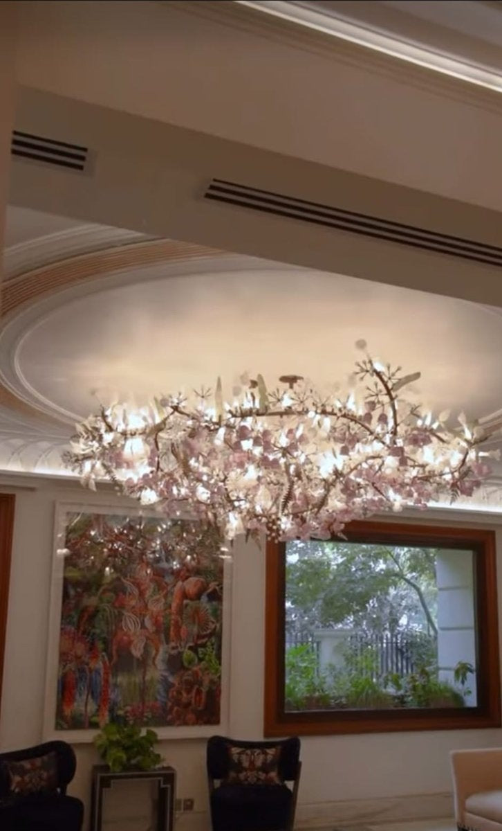 Canopy chandelier with bronze-toned metal branches covered in illuminated blush-pink and white glass blossoms beneath a circular ceiling cove