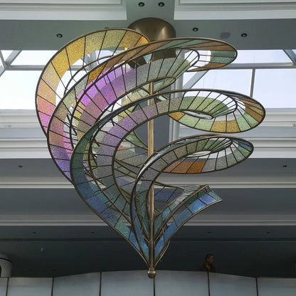 Full view of the spiral bronze-framed chandelier with pastel gold, violet, green, and blue textured glass ribbons under a skylight