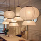 Close-up cluster of five glowing white ribbed silk-paper tiered lantern pendants combining globe, cylinder, and open dome shades over a dining table