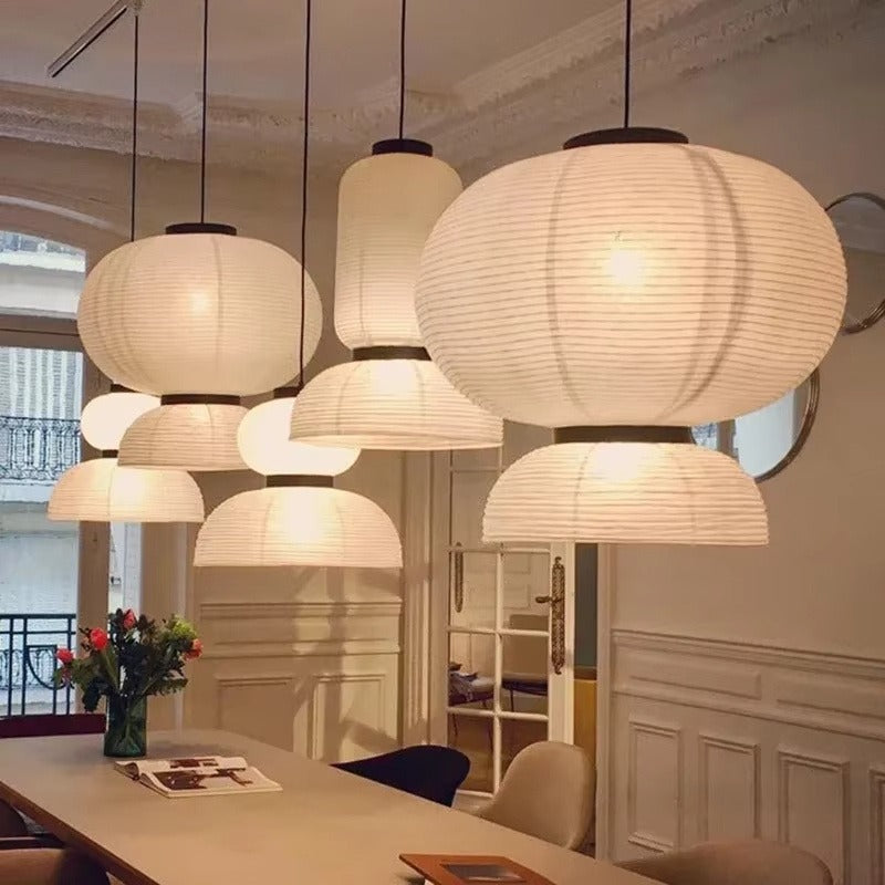 Close-up cluster of five glowing white ribbed silk-paper tiered lantern pendants combining globe, cylinder, and open dome shades over a dining table