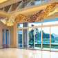 Wide view of the sweeping amber and gold glass wave chandelier suspended above a polished marble floor near garden windows