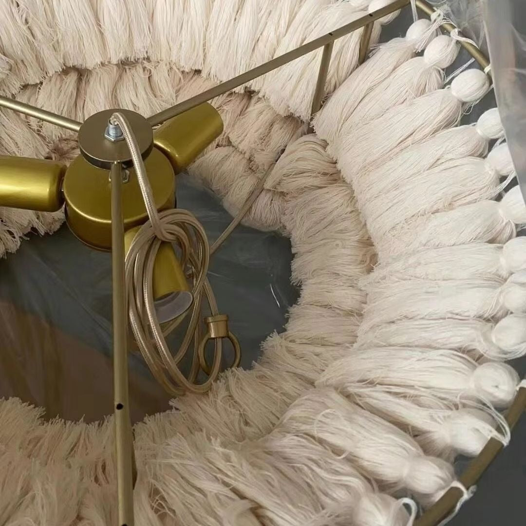 Close-up interior view of the brushed brass ring frame, central lamp holders, braided cord, and hand-tied cream cotton tassels