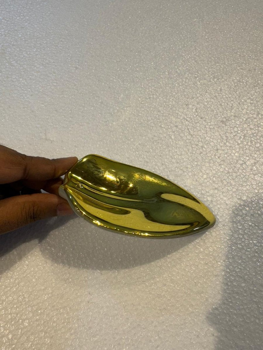 Close-up of a single sculpted curved glass leaf element finished in a reflective metallic gold glaze