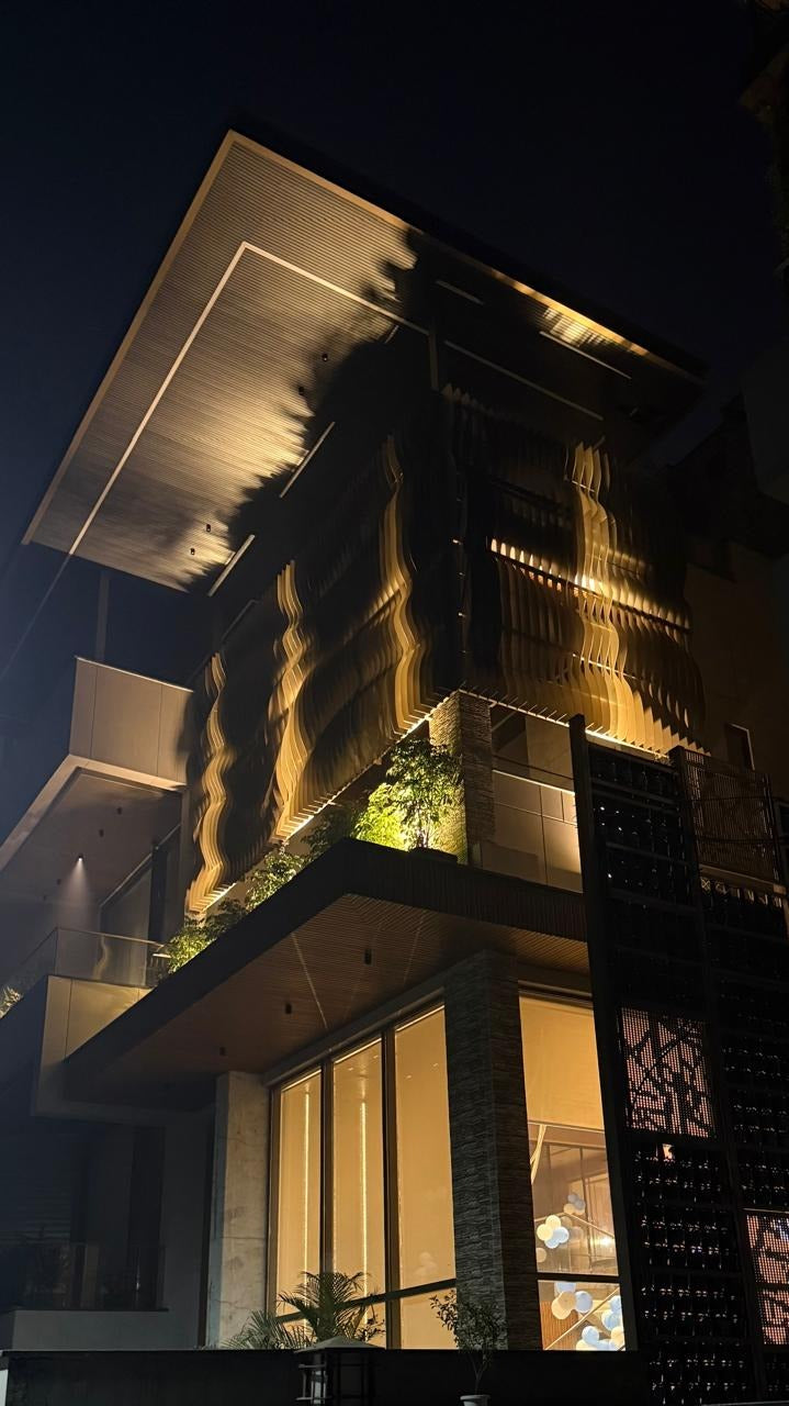 Wavy metal facade fins lit from below by narrow-beam up-lights, with LED outlines along the soffit