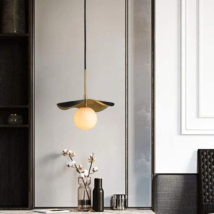 Single brass lotus leaf and white alabaster sphere pendant chandelier suspended above a console table with cotton stems