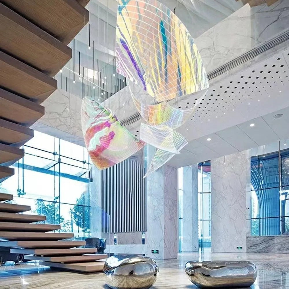 Wide view of the multi-panel iridescent mesh chandelier hanging beside a modern floating wooden staircase in a marble lobby