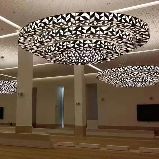 Angled view of tiered concentric geometric ring chandeliers showing triangular dark bronze metalwork and illuminated frosted glass panels