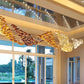 Opposite-angle perspective of the twisting cognac, amber, and clear champagne glass cylinder ribbons hanging from a mirrored tray