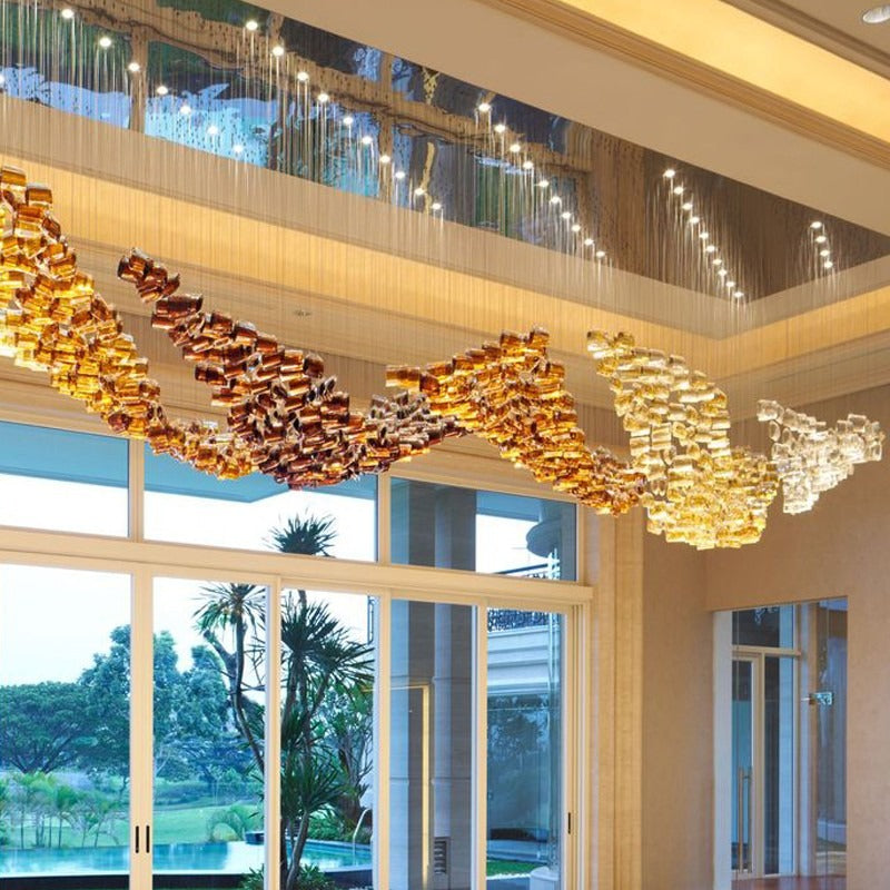 Opposite-angle perspective of the twisting cognac, amber, and clear champagne glass cylinder ribbons hanging from a mirrored tray