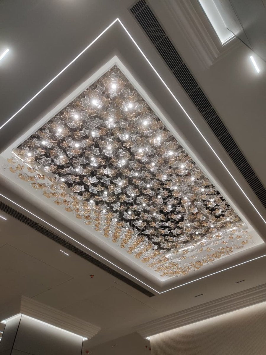 Perspective view of the clear and amber glass blossom cluster chandelier glowing against its mirrored ceiling plate