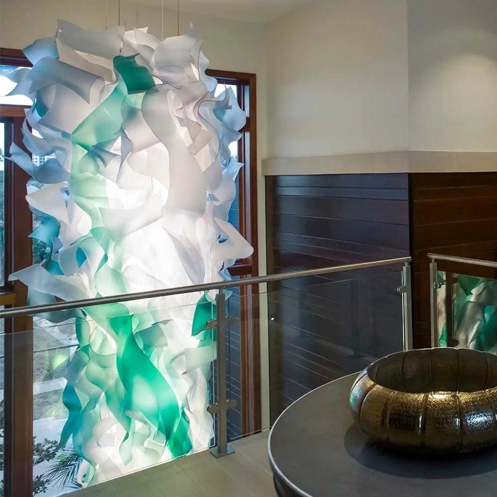 Mezzanine view of the illuminated white and green wave-ribbon chandelier rising beside a glass and steel balustrade
