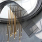 Detailed view of the arching black wire-slat ribbon alongside glowing brushed-brass vertical tube drops