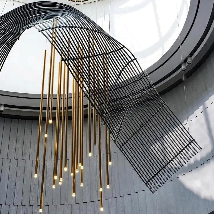 Detailed view of the arching black wire-slat ribbon alongside glowing brushed-brass vertical tube drops