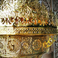 Macro detail of the pierced brass rosette medallions, lattice bands, and scrollwork brackets on the chandelier body