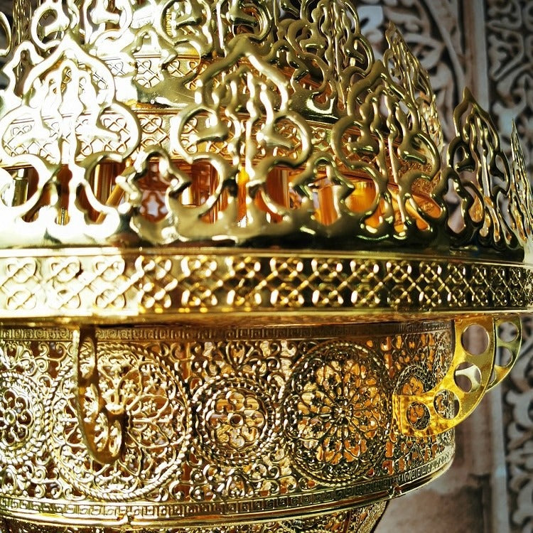 Macro detail of the pierced brass rosette medallions, lattice bands, and scrollwork brackets on the chandelier body