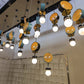 Wide view of the staggered cluster of perforated mesh drum and opal globe pendants hanging across a lounge ceiling