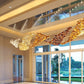 Three-quarter view of the long rectangular ceiling trough with the gradient gold and amber glass wave sculpture in a grand hall