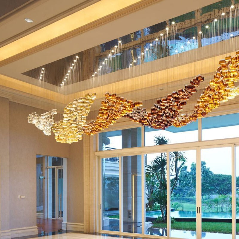 Three-quarter view of the long rectangular ceiling trough with the gradient gold and amber glass wave sculpture in a grand hall