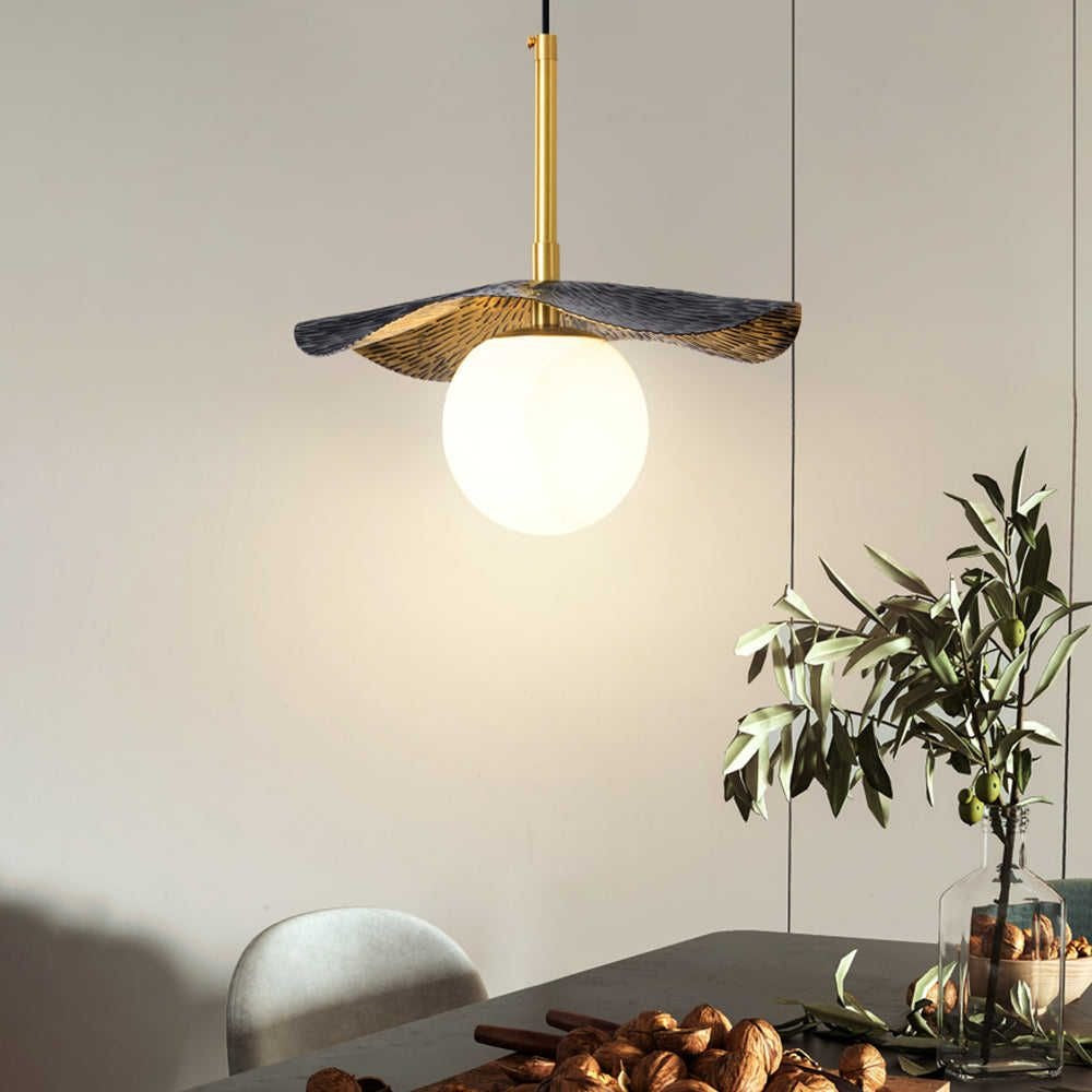 Illuminated brass lotus leaf and alabaster globe pendant light hanging over a modern dining table with olive branches
