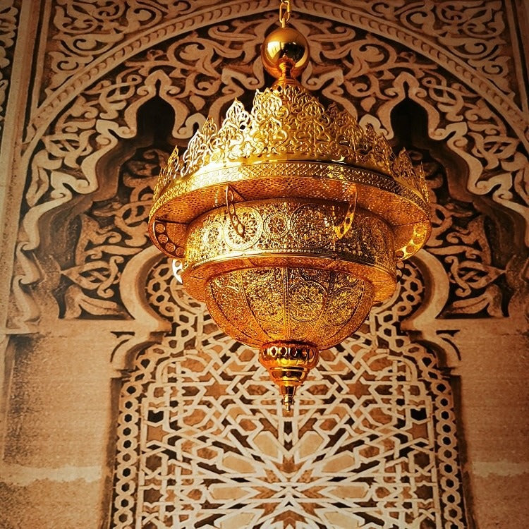 Low-angle view of the tiered golden filigree dome chandelier with its tapered bottom finial against patterned stonework