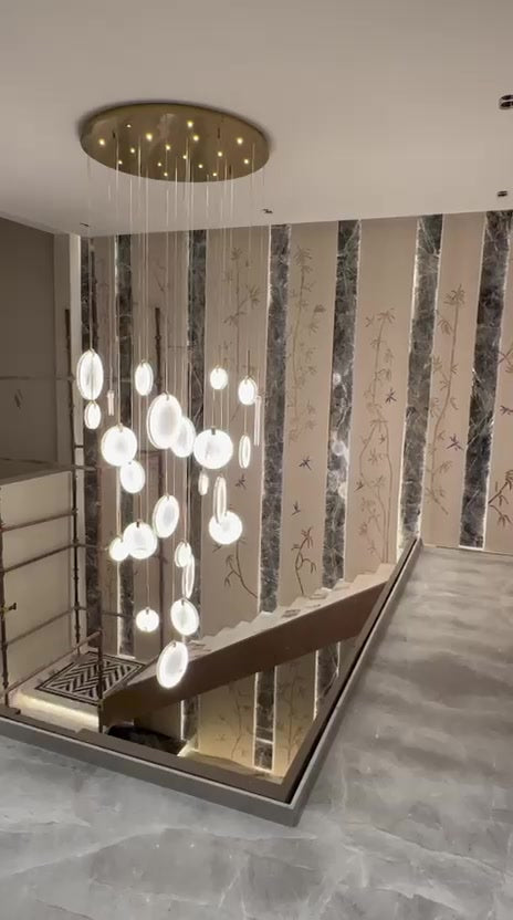 Glass-disc cluster chandelier hung at different heights from a round gold canopy in the double-height lobby