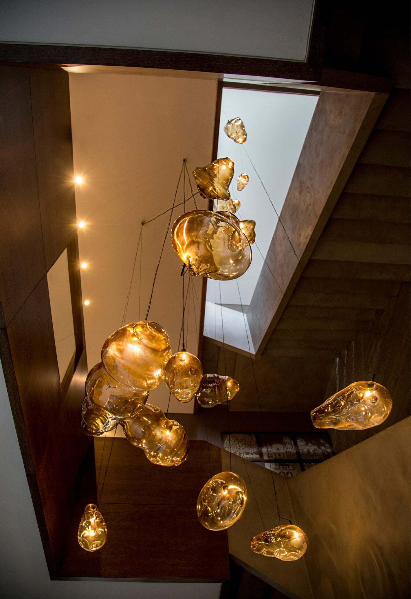 Molten amber hand-blown glass bubble cluster chandelier installed above a staircase, double-height space