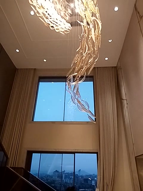 Full drop of the feather glass chandelier past the tall windows of the double-height living room