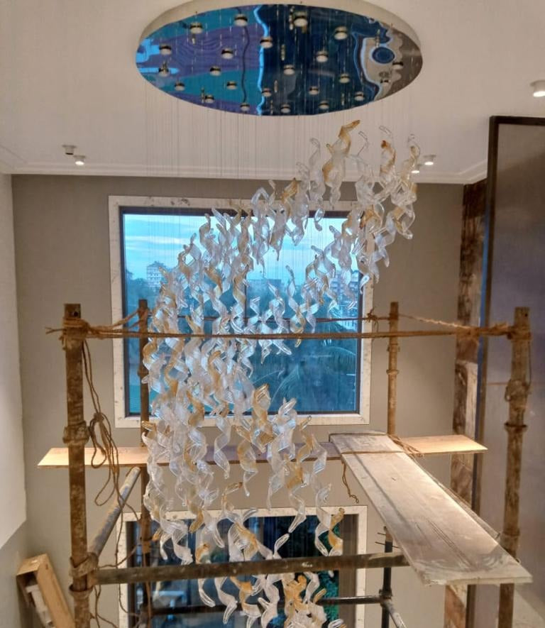 Clear and amber twisted glass ribbon chandelier being installed from scaffolding in the same Guwahati home