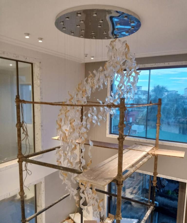 Glass ribbon spiral hanging from its round mirrored canopy across the double-height void, during installation