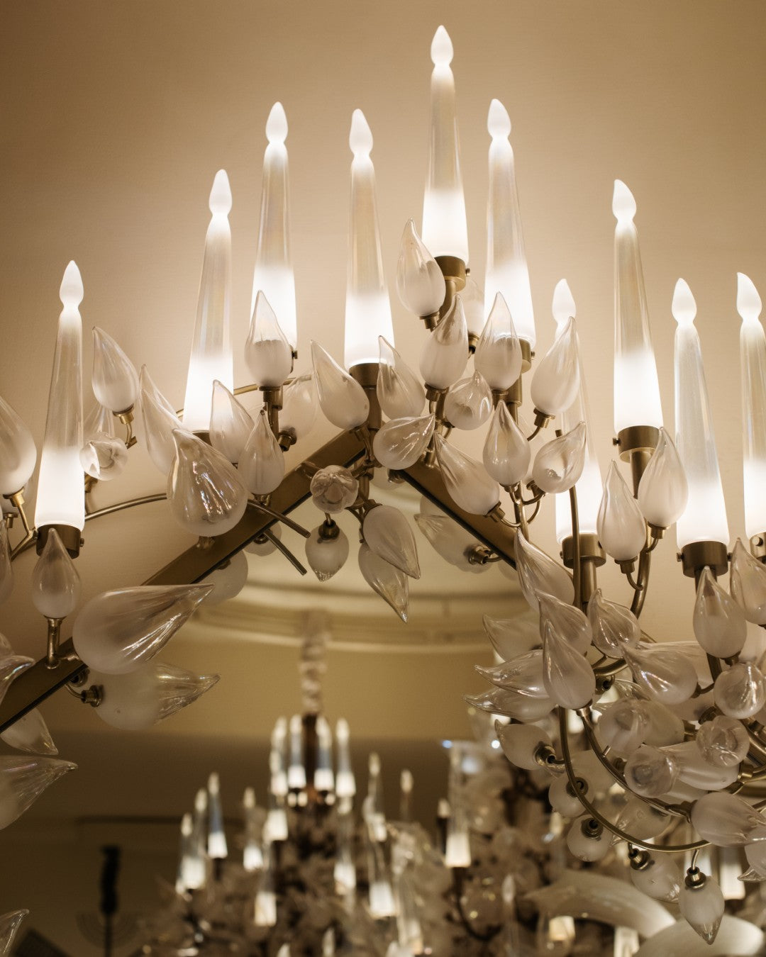Close-up detail of hand-blown frosted glass leaves and candle-flame diffusers on the chandelier's brass branch frame