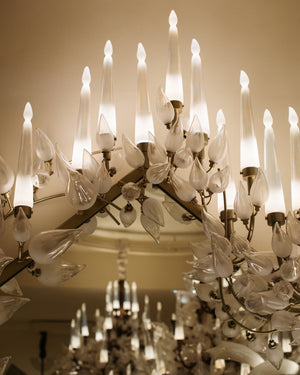 Close-up detail of hand-blown frosted glass leaves and candle-flame diffusers on the chandelier's brass branch frame