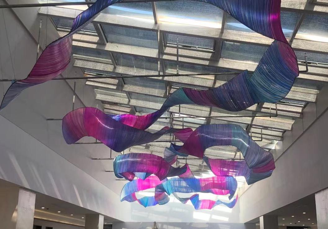 Chromatic gradient ribbon sculpture chandelier sweeping across a skylit ceiling