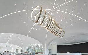 Coiled brass ring chandelier with illuminated rings spiraling from wide to narrow over a double-height space