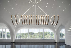Coiled brass ring chandelier with illuminated rings spiraling from wide to narrow over a double-height space