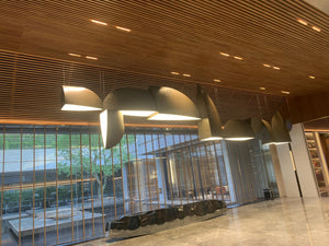 Bronze sail-form pendant chandelier with curved metal panels staggered along a wood-panelled reception ceiling
